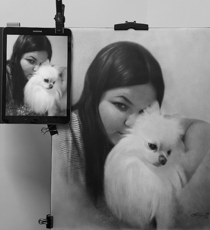 Hyper-realistic portrait in pencil of a woman with her dog, displayed beside a tablet showing the same image.