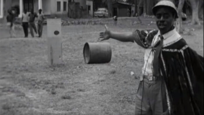Man in historical attire gestures outdoors with a barrel in the background. Grasshoppers context.