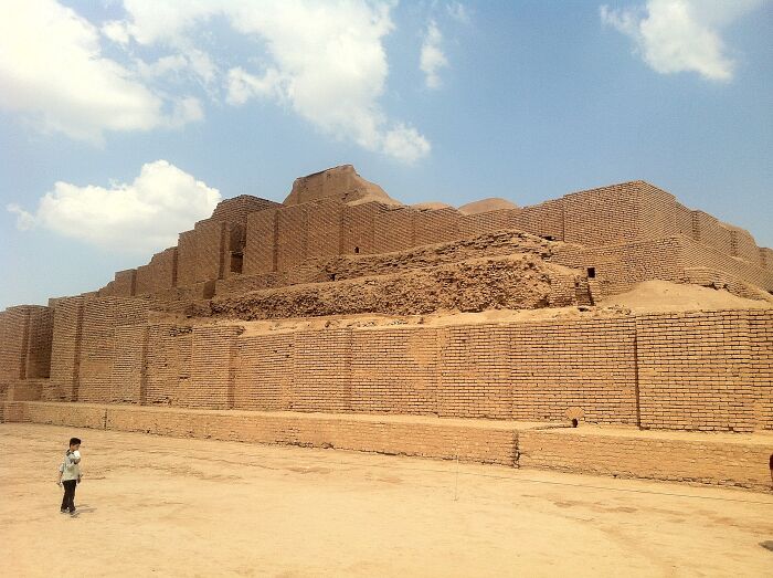 Ancient architectural wonder, made of mud-brick layers, with a person in the foreground under a clear blue sky.