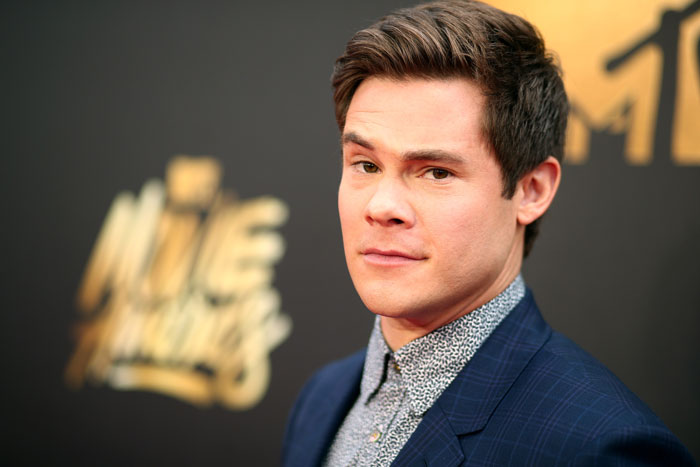 Actor from 'Pitch Perfect' on a red carpet, wearing a dark blue suit and patterned shirt.
