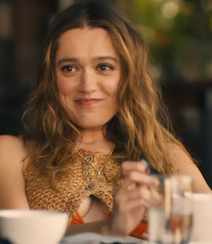 Woman smiling with long hair, wearing a textured top, sitting at a table.