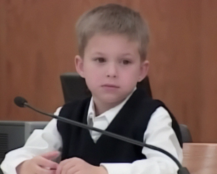 Young boy in a courtroom setting, wearing a vest and white shirt, related to the life sentence story.
