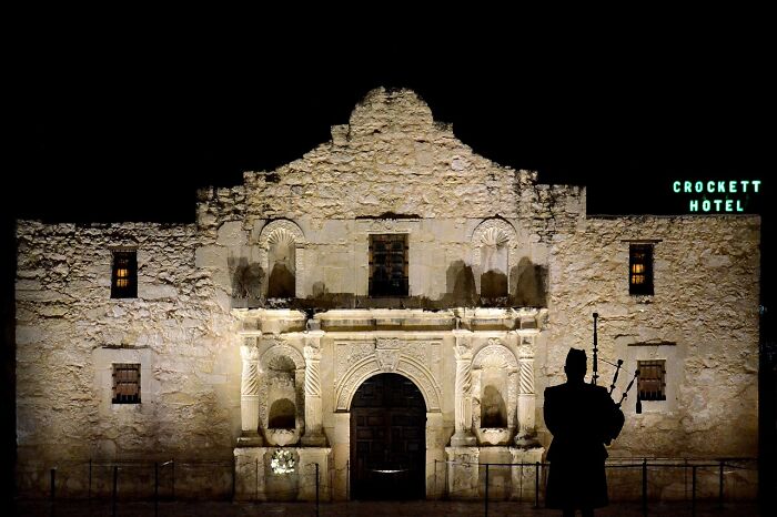 Historic building at night with a bagpiper silhouette and Crockett Hotel sign, reflecting tourist experiences.