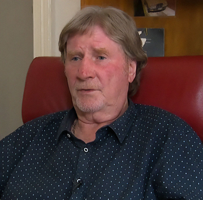 Man in a polka dot shirt sitting on a red chair, linked to a family mystery about burial location disclosure.