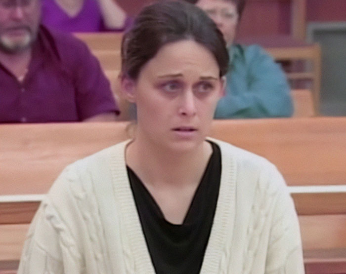 Woman sitting in court with a worried expression, wearing a white sweater.