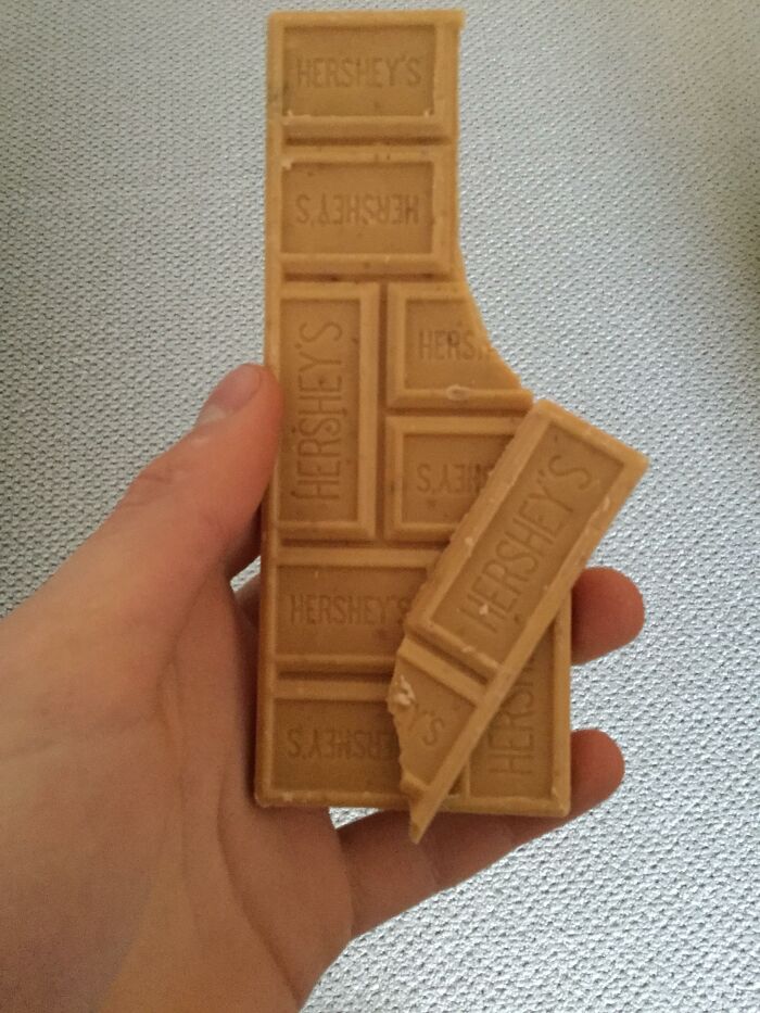 A hand holding a Hershey's chocolate bar with some pieces broken off, highlighting American food available internationally.