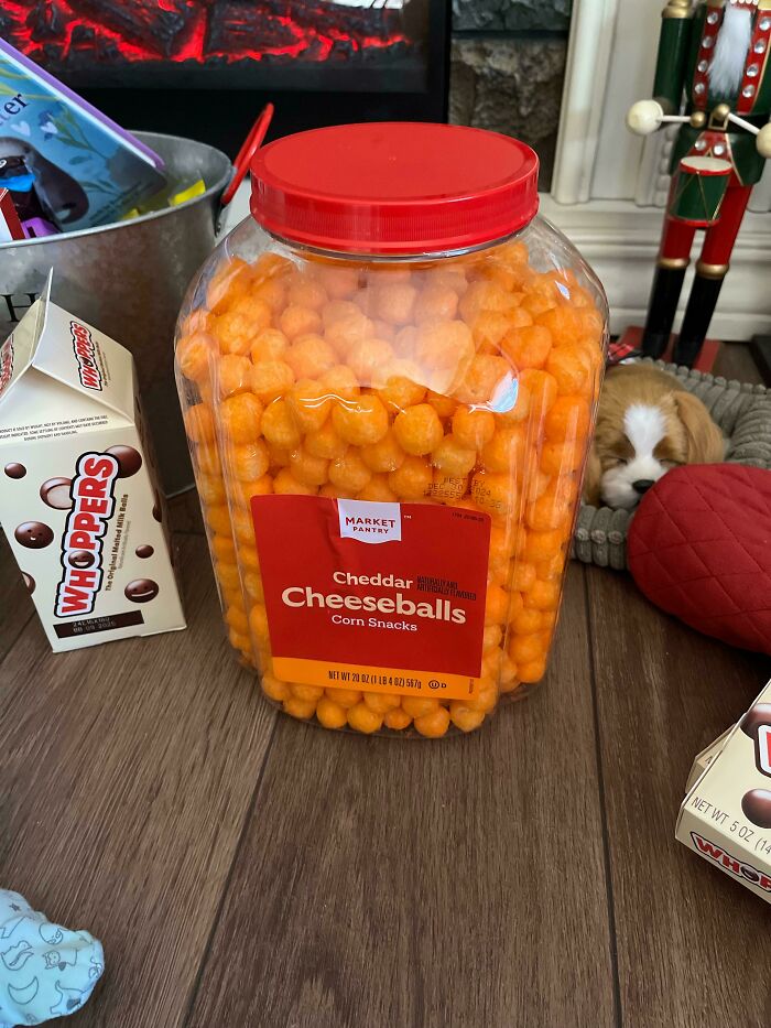 Jar of American cheese balls and box of Whoppers on a wooden floor.