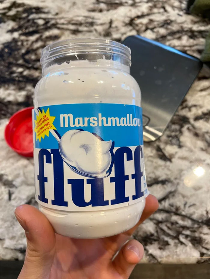 Jar of Marshmallow Fluff, a popular American food, held in a kitchen setting.