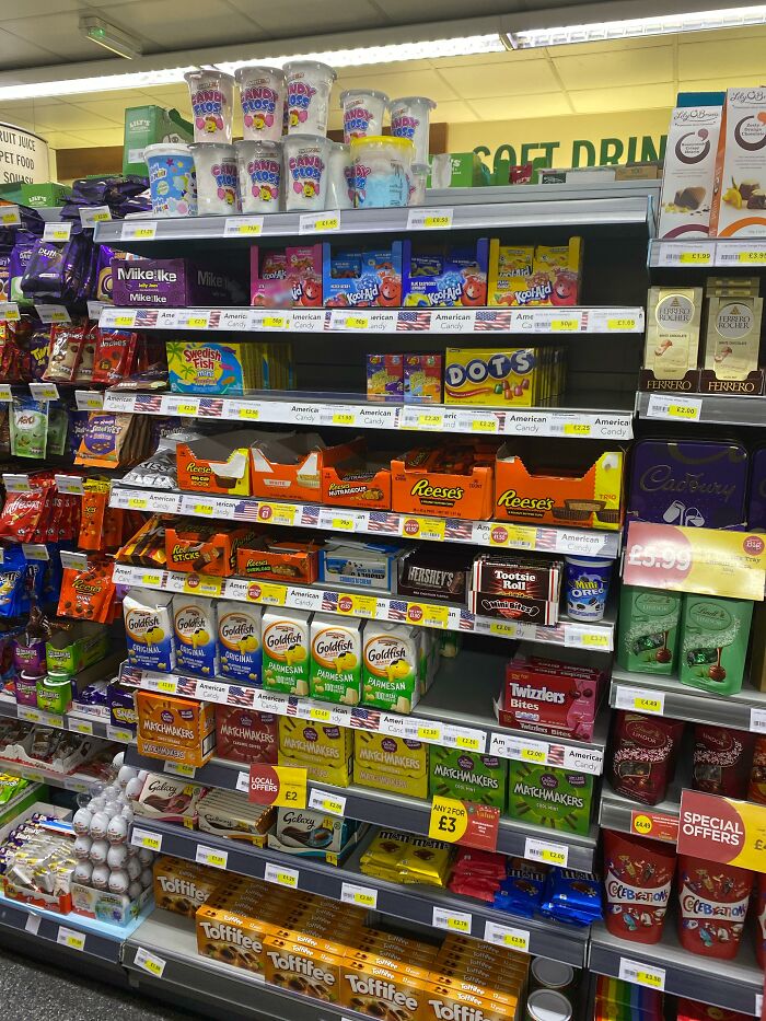 A store shelf displaying American food products like candy, snack packs, and chocolate bars available for purchase.