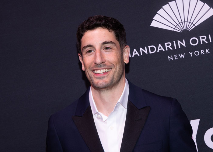 Actor in NYC event showcasing significant weight loss, smiling in a suit against a branded backdrop.