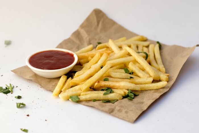 French fries with ketchup on brown paper, typical American snack.
