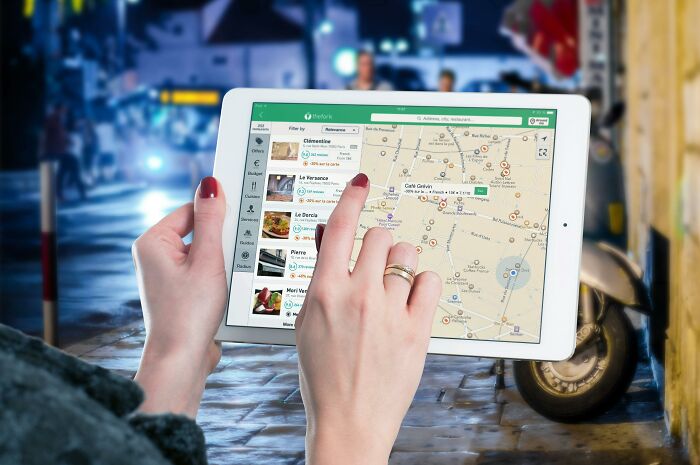 Hands holding a tablet displaying a map in a busy street, indicating a tourist navigating through a city.