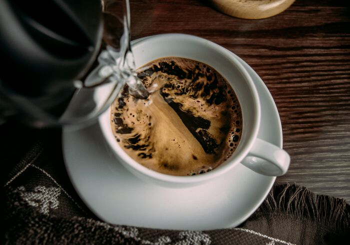European coffee being poured into a white cup on a wooden table.