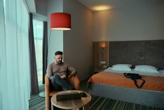 Man sitting in hotel room with phone, reflecting on reasons why guys slept with a married woman in a quiet setting.