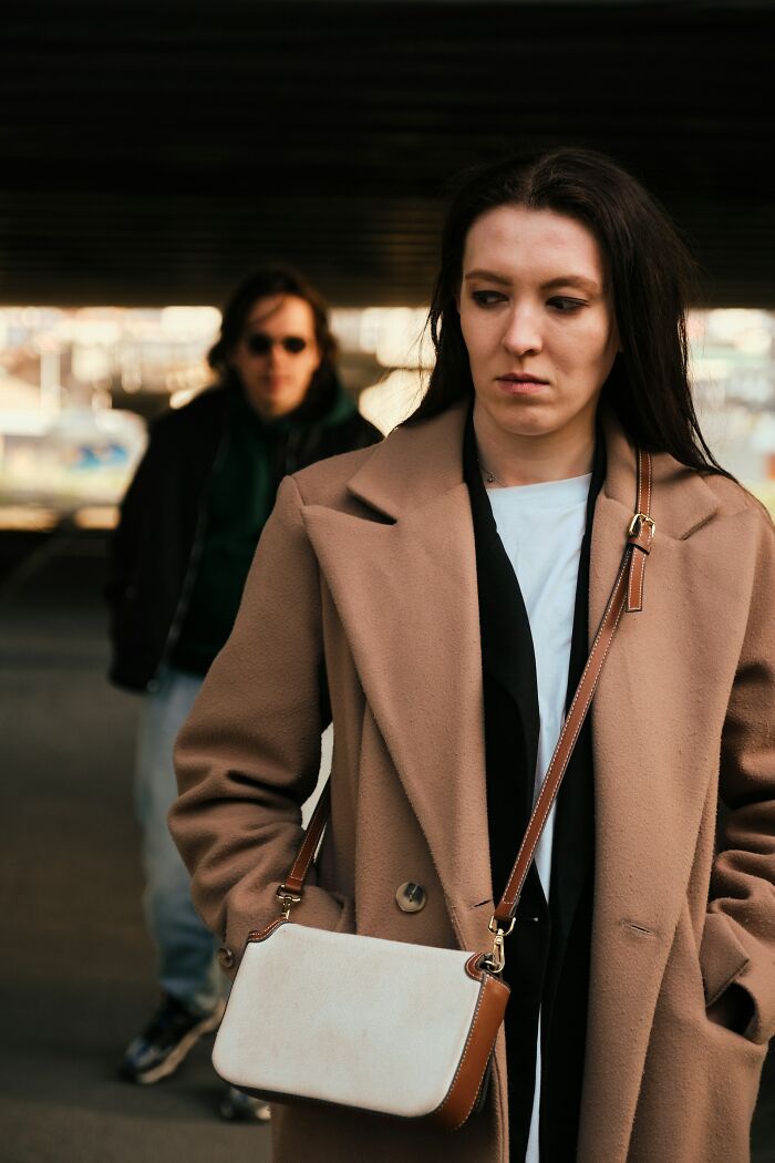 A woman in a coat looking uneasy with a man approaching from behind, illustrating a potentially traumatizing encounter.