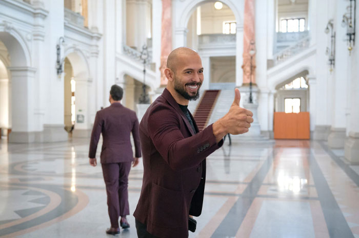 Andrew Tate gives a thumbs up in a grand hall, highlighting discussions around net worth.