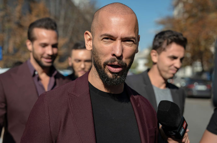 Andrew Tate speaking into a microphone outdoors, discussing Andrew Tate's net worth with a serious expression.