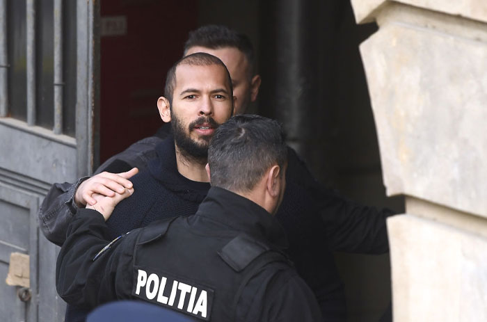 Andrew Tate being led by police officers, highlighting debate over net worth.