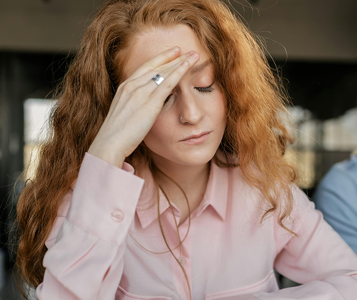 Concerned woman with hand on forehead, wearing a pink shirt, illustrating anxiety over diseases.