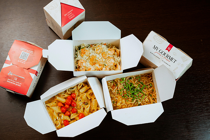Takeout meals from My Gourmet, featuring pasta and noodles in white boxes on a dark table. Takeout meals from My Gourmet, featuring pasta and noodles in white boxes on a dark table.
