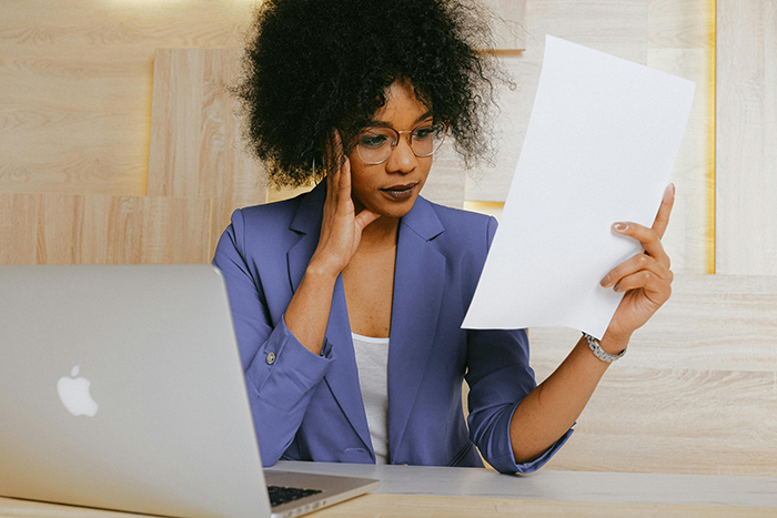 Woman in purple blazer reading a document at a desk with a laptop, contemplating issues about marriage and name decisions.