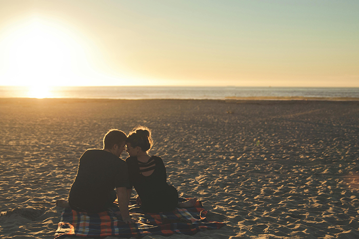 Couple sitting on a beach at sunset, illustrating themes of relationships and marriage discussions.