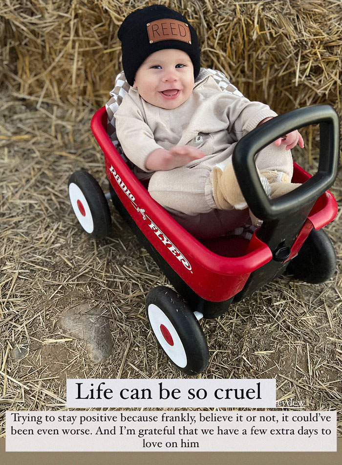 Toddler smiling in a red wagon, wearing a black hat.