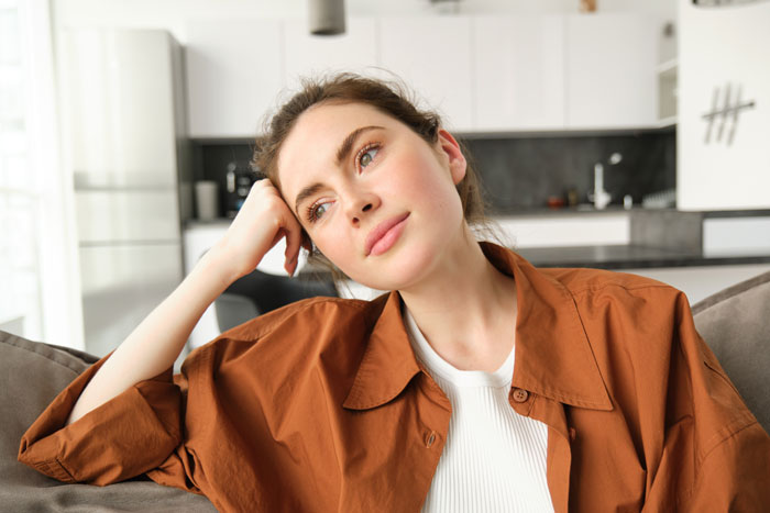 Young woman with a thoughtful expression sitting on a couch, reflecting on babysitting and payment fairness issues.