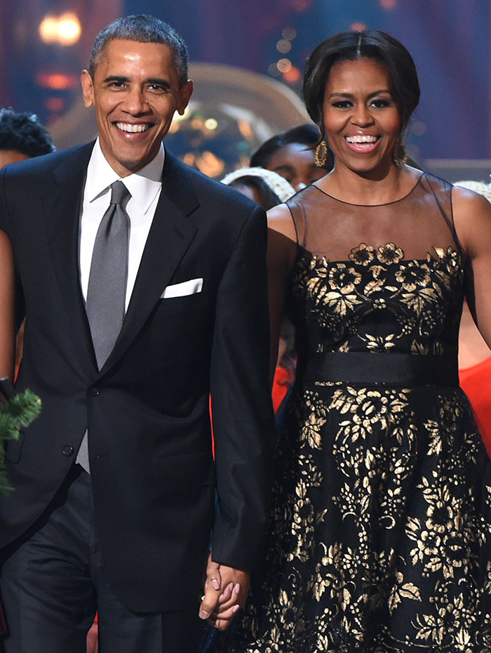 A couple holding hands, both smiling, in formal attire, attending a public event.