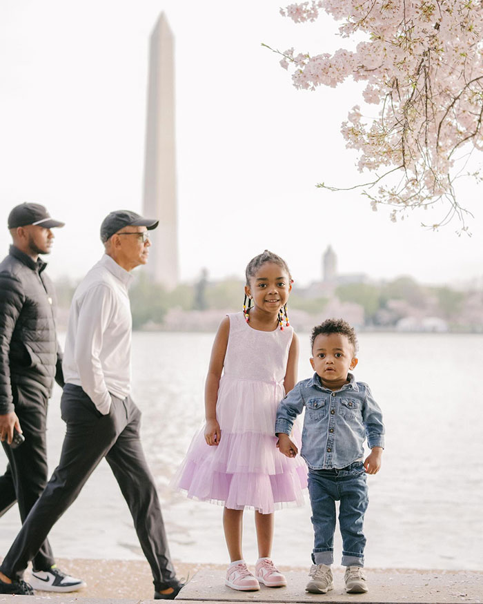 Barack Obama photobombs kids' photo shoot by a lake, with cherry blossoms and the Washington Monument in the background.