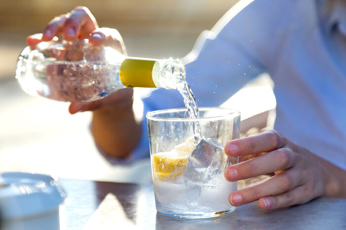 Person pouring bottled water into a glass with ice and lemon, highlighting differences Americans find in Europe.