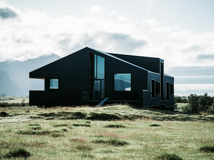 A modern black house in a remote field with cloudy skies, showcasing impractical yet visually appealing home architecture.