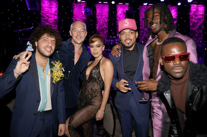 Group of artists including Benny Blanco at a stylish event, dressed in formal attire, with a vibrant party backdrop.