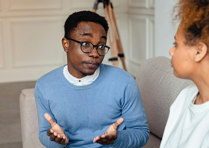 Man in blue sweater talking to woman, discussing wedding bet situation.