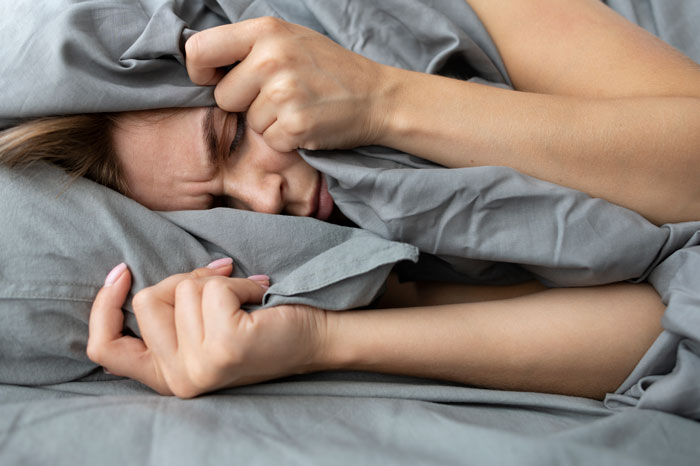 Woman struggling with lack of proper sleep, covering face with pillow, showing signs of stress and exhaustion in bed. Woman struggling with lack of proper sleep, covering face with pillow, showing signs of stress and exhaustion in bed.