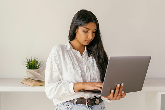 Woman using laptop at home office, contemplating medical expertise.