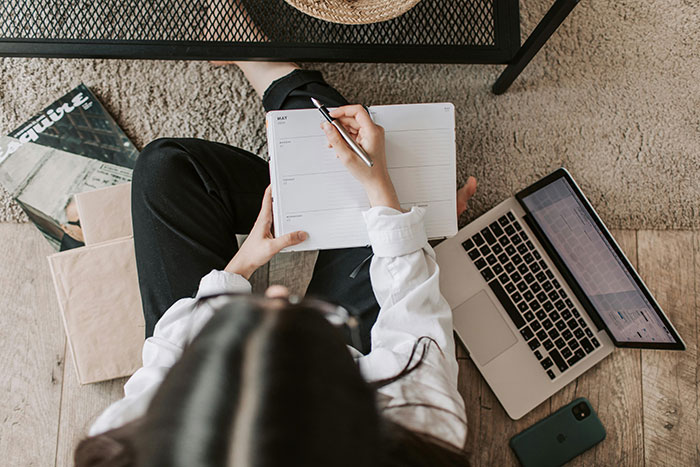 Woman reviewing notes at home, seated by a laptop with magazines nearby, reflecting on medical expertise challenges.