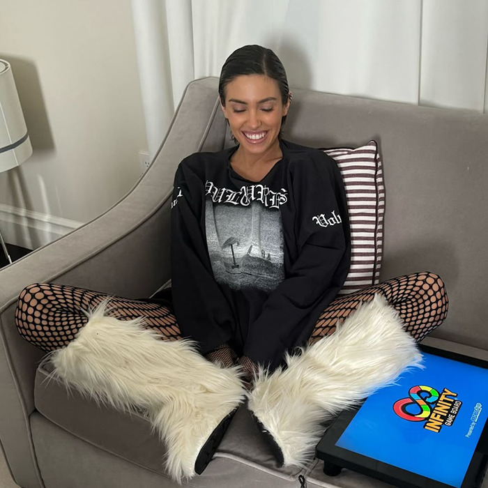 Woman seated on sofa in a relaxed pose with furry boots, smiling, phone nearby.