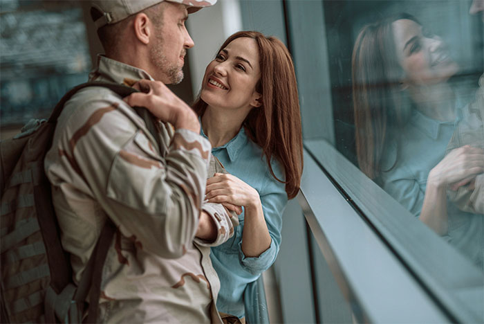 Man in military uniform embraces smiling woman by a window, illustrating marriage themes.