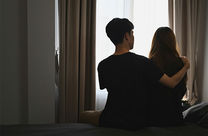 Man sits next to wife by window, reflecting on relationship.