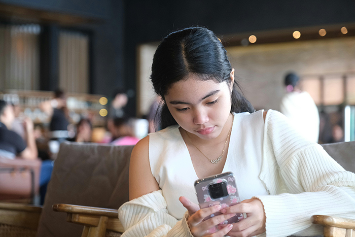 Young woman in a cafe using a smartphone, surrounded by a cozy atmosphere.