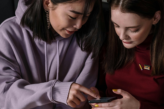 Two women looking at a phone together, engaged in conversation about a vacation ban.