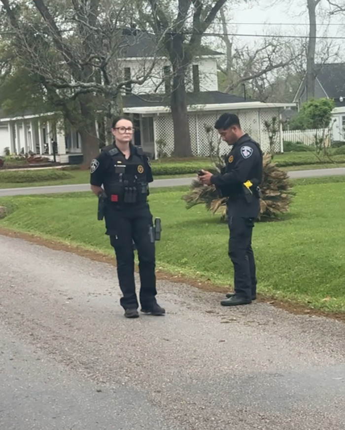 Police officers standing in a residential street, with a house in the background.