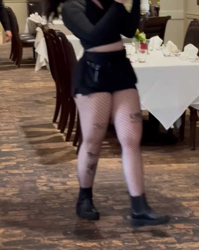 Woman in a restaurant wearing a black outfit, central to a lawsuit over dress code enforcement.