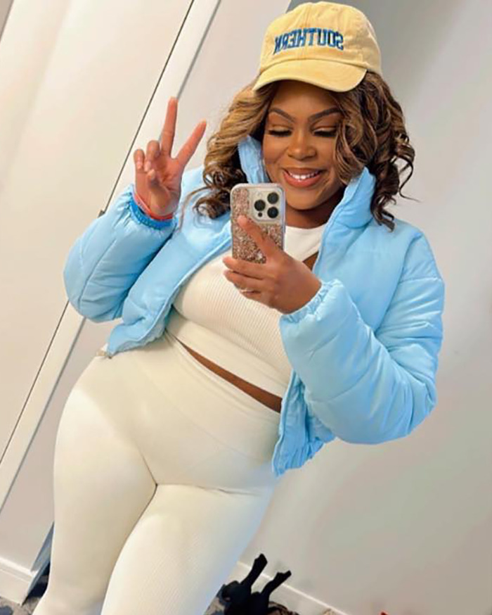 Woman sues restaurant, poses in mirror wearing a blue jacket and beige outfit, smiling with a peace sign.