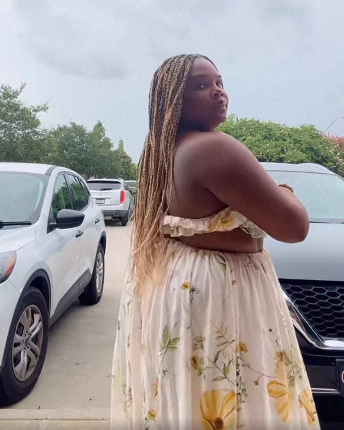 Woman in floral dress stands in parking lot, central to dispute involving a restaurant and "revealing" outfit.