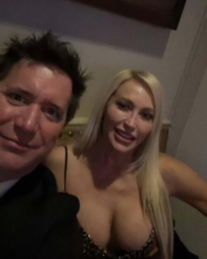 Two people posing for a selfie in a restaurant, focusing on the woman's controversial outfit.