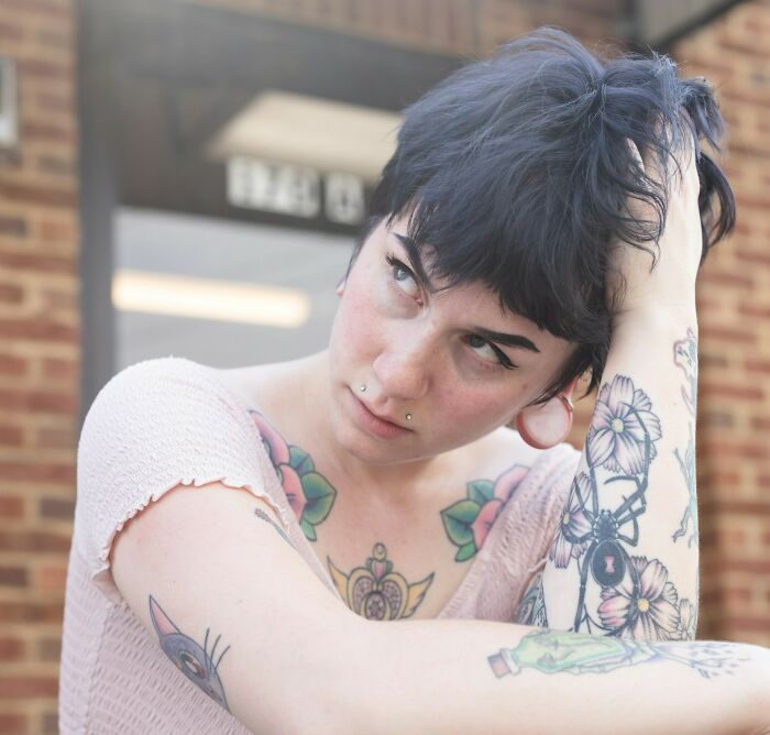Young woman with tattoos looking thoughtful, representing women discussing partners in relationships.