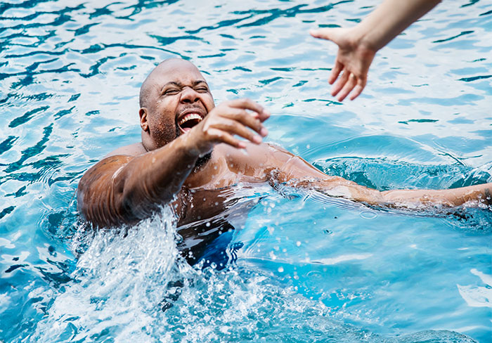 Man struggling in water reaching for lifeguard&rsquo;s outstretched hand during a near drowning rescue at the pool.