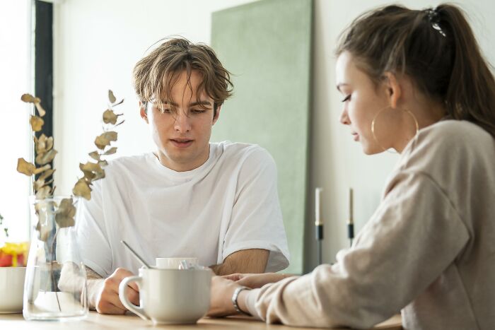 Young couple having a serious conversation at a table, showing tension related to paying and jealousy issues in their relationship.